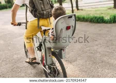 A young father carries his little son in a bicycle seat. dad and son ride a bike. Child safety concept Royalty-Free Stock Photo #2170924547