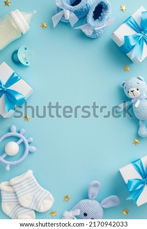 Baby concept. Top view vertical photo of gift boxes shoes socks pacifier teddy-bear teether bottle knitted bunny rattle toy gold stars on isolated pastel blue background with copyspace in the middle