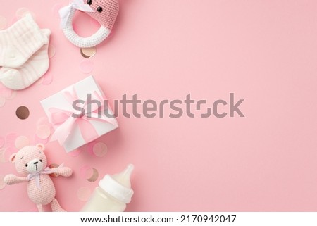 Baby accessories concept. Top view photo of knitted bunny rattle toy giftbox tiny socks teddy-bear toy milk bottle and shiny confetti on isolated pastel pink background with copyspace