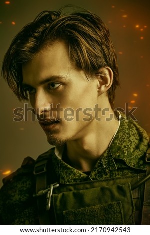 Portrait of a furious, courageous soldier in camouflage looking resolutely away. War, battle with the enemy. Studio portrait on a dark gray background with sparks.  Royalty-Free Stock Photo #2170942543