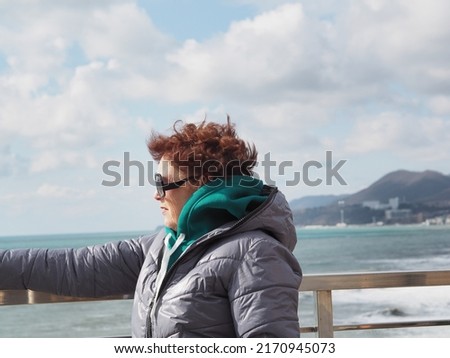 Portrait of an elderly woman against the backdrop of cold weather on the Black Sea. Windy and inclement weather. Walking outdoors in any weather.