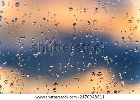 Raindrops on a window with a sunset sky in the background. Clear weather after the rain.