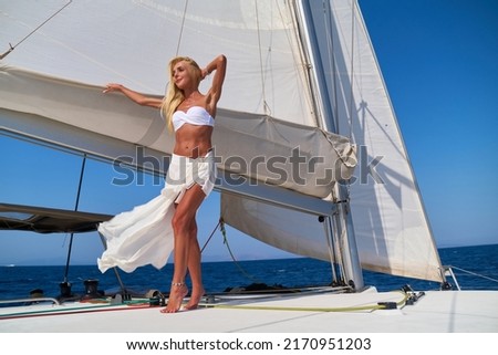 Beautiful young blond woman in bikini standing on catamaran at sunny summer day