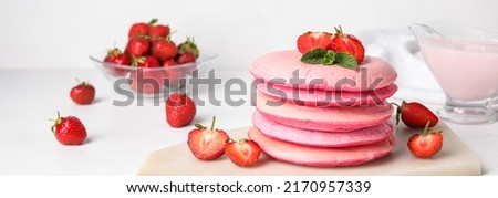 Tasty pink pancakes with strawberry on light background