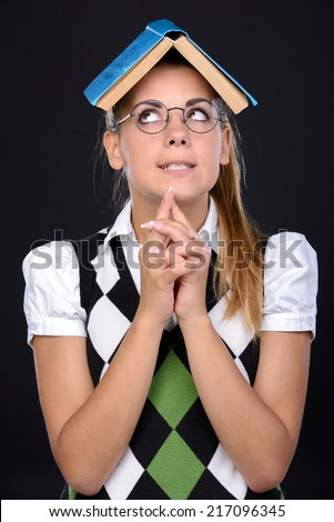 Young nerd woman crazy expression in glasses, holding book on head on black background