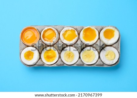 Boiled chicken eggs of different readiness stages in carton on light blue background, top view Royalty-Free Stock Photo #2170967399