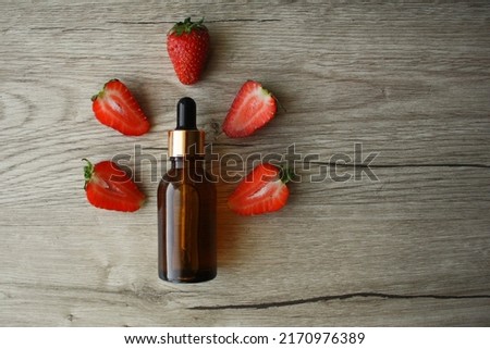 Aroma and flavor enhancer next to ripe strawberries, on wooden background. Strawberry essential oil isolated on wooden background.