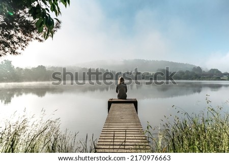 Calm misty morning meditation by pond.Sitting woman outdoors.Wellbeing and wellness soul concept.Spring foggy nature.Silence.Woman feeling freedom,enjoying vacation.No stress,calm mind,relax Royalty-Free Stock Photo #2170976663