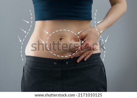 Skinny fat woman figure in fitness clothes touches stomach. Abdominal fat and dieting concept. Massaging marks. Royalty-Free Stock Photo #2171010125