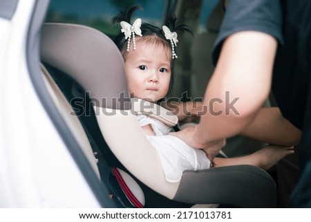 Little baby fastened with security belt in safety car seat. Toddler girl buckled into her car seat. Adorable little girl sitting in car. Image of safety before drive car.