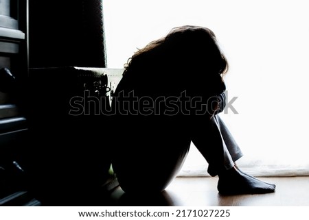 Unhappy mature lady, woman in silhouette, sitting on the floor with back lit. Depressing thoughts. 