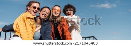 joyful multicultural friends in stylish sunglasses looking at camera outdoors, banner