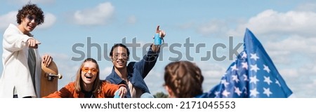 smiling skater pointing at woman with usa flag near interracial friends with soda cans, banner Royalty-Free Stock Photo #2171045553