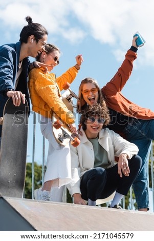 asian skater pointing at overjoyed friends screaming with raised hands outdoors Royalty-Free Stock Photo #2171045579