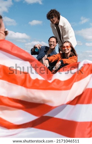 smiling interracial friends looking at woman with usa flag on blurred foreground