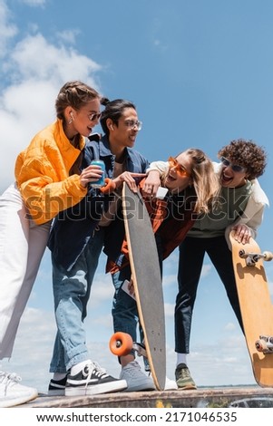laughing friends looking at asian skater grimacing and pointing with finger outdoors Royalty-Free Stock Photo #2171046535
