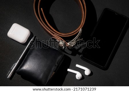 set of men's stuff on black background. smartphone, wireless earphone, leather belt, leather wallet and ballpoint pen