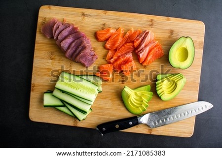 Slicing Fresh Fish and Vegetables to Make Sushi: Sliced fish, avocado, and cucumber on a bamboo cutting board Royalty-Free Stock Photo #2171085383
