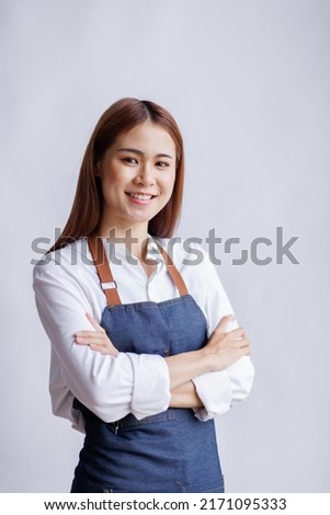Young Asian woman wearing apron isolated on white background with copy space. Portrait of successful Asian woman with crossed arms on a white wall. Smiling young waitress looking at camera.