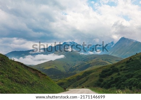 Road across green hills and colorful mountains, surrounded by low clouds