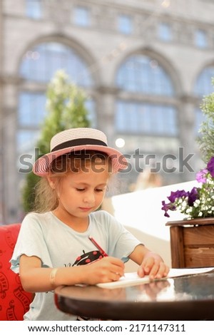A little girl in a hat draws in a street cafe