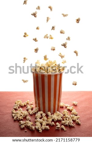 popcorn bucket full, with popcorn floating in the air and on the red table with white background vertical picture