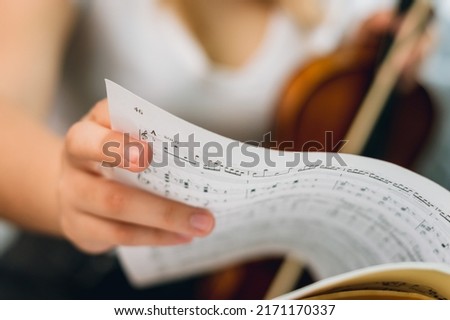 close up Caucasian female hand turning page of sheet music on music stand, woman violinist blurred in background, with copy space.