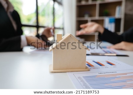Close up and focus of house model mock up on the table and paperworks that shows graft and chart of accounting and financial. Business women hands are discussed worked.