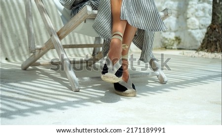 European girl's legs in a dress sitting in shoes on chair on backyard