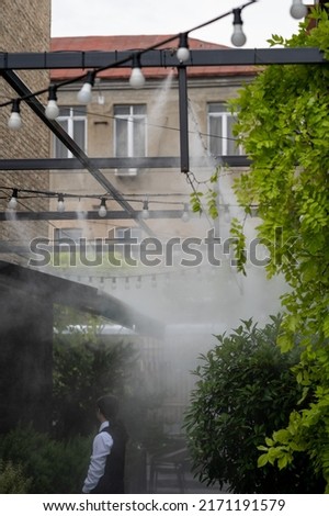 Air conditioning and water spray system for cooling and fog. Fogging system for outdoor cafe terraces. Humidify, cooling and cleaning air from dust in hot day. Air humidification for plants in summer Royalty-Free Stock Photo #2171191579