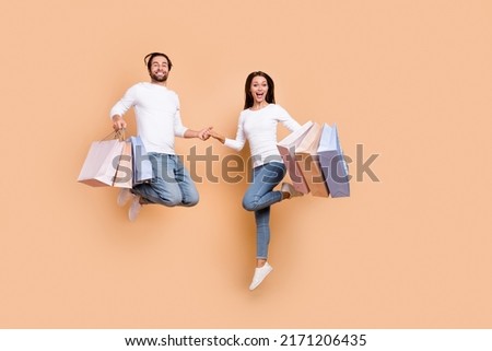 Full length body size view of beautiful handsome trendy friends jumping carry purchase isolated over beige pastel color background