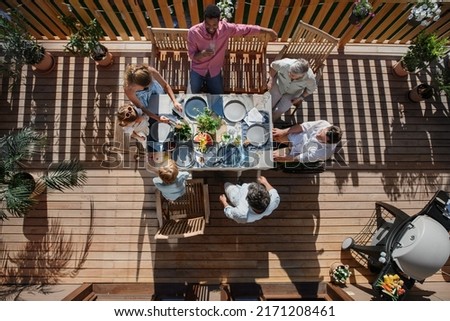 Top view of 3 generations family eating at barbecue party dinner on patio, people sitting at table on patio with grill.