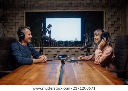 Young woman host talking to microphone and interviewing a man for a radio podcast.