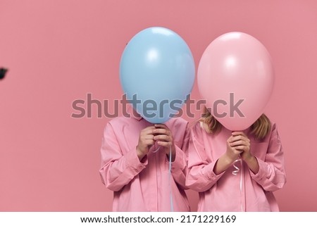 school-age children stand holding balloons in their hands, covering their faces with them. Horizontal photo on an empty pink background with space for inserting advertising text