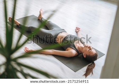 Young fit woman practice yoga doing savasana in light yoga studio with green house plant Royalty-Free Stock Photo #2171256911