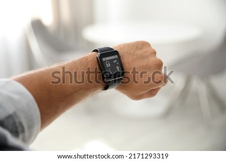 Young man showing electronic wristwatch with Smart Home Interface indoors, closeup