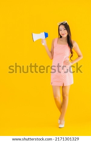 Portrait beautiful young asian woman speak loud with megaphone on yellow isolated background