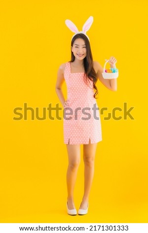 Portrait beautiful young asian woman with bunny ears with easter eggs in basket on yellow isolated background