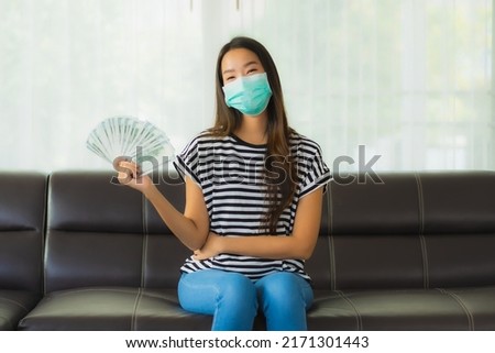 Portrait beautiful young asian woman with mask on sofa show money or cash at home Royalty-Free Stock Photo #2171301443