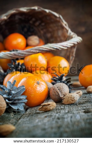 Composition with Basket, Food, Fruits and Nuts. Tangerines, Pine cones, Walnuts, Almonds are scattered on wooden background. Rural christmas style