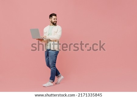 Full body young smiling man 20s in trendy jacket shirt hold use work on laptop pc computer look aside on workspace area isolated on plain pastel light pink background studio. People lifestyle concept Royalty-Free Stock Photo #2171335845