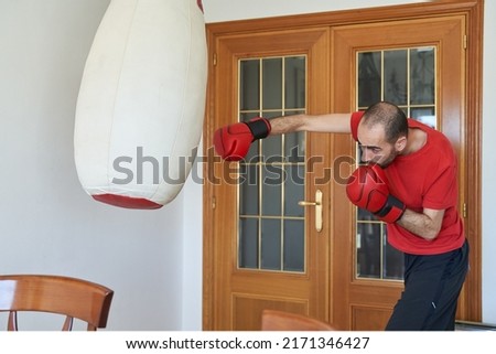 Conditioning boxing training at home. Young male hits jab in living room to heavy bag