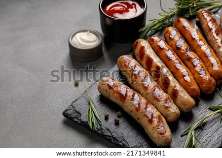Grilled assorted sausages with sauces and rosemary. Homemade sausages on a stone board. Dark background. Copy space. Royalty-Free Stock Photo #2171349841