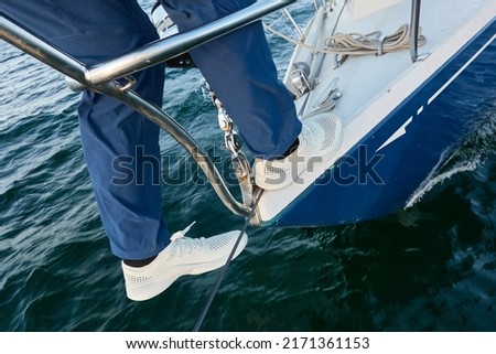 Man in a blue jeans and white boots standing on deck of a sloop rigged yacht. Baltic sea. Healthy lifestyle, sport, recreation, cruise, vacation, regatta, sailing lessons, leisure activity, wanderlust Royalty-Free Stock Photo #2171361153