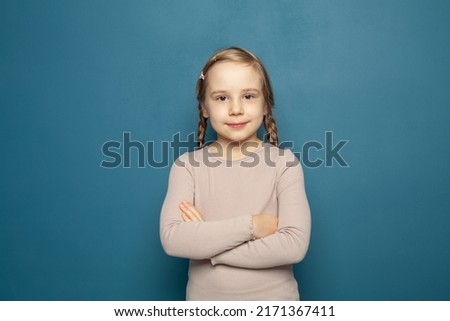 Close up head shot portrait with smiling little brown-haired girl. Happy beauty kid on blue background, seven year child looking at camera and posing