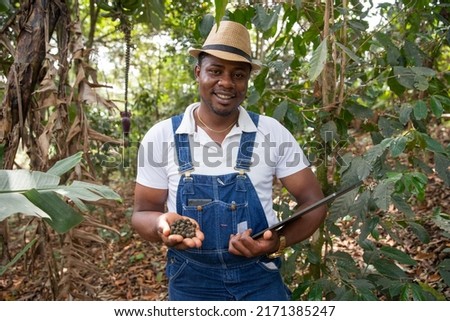 African farmer in his coffee plantation with coffee beans in his hand and a tablet Royalty-Free Stock Photo #2171385247