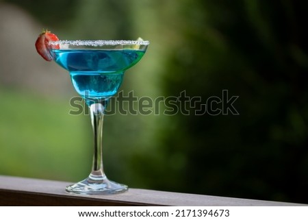 Glass with blue margarita cocktail garnished with lime zest and strawberries, selective focus