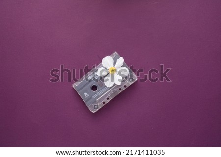 A cassette  from the middle of witch a  white flower emergens on purple background