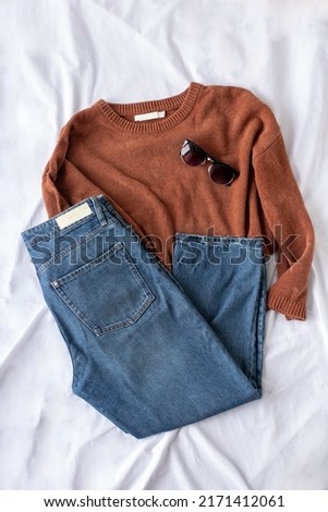 Clothing women flat lay with blue jeans, brown sweater, black sunglasses on white