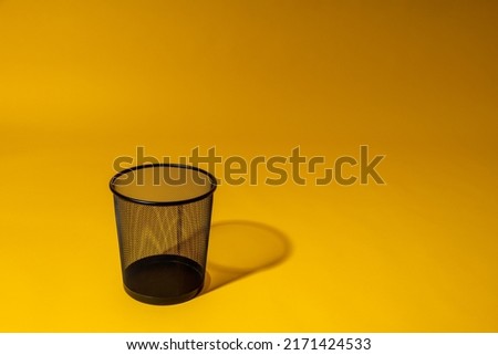 Waste basket close-up isolated on yellow background. Office metal black mesh bin.